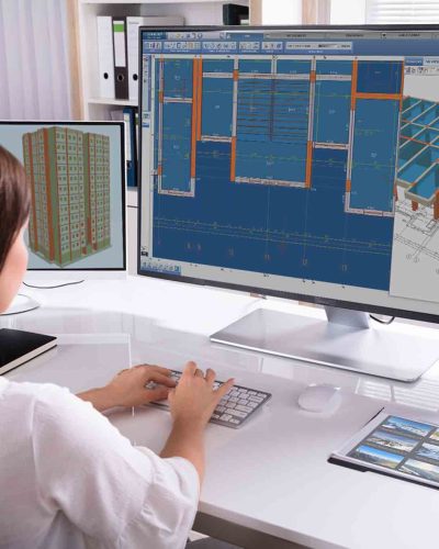 Beautiful Brunette Female Video Editor Works with Footage on Her Personal Computer with Big Display. She Works in a Cool Office Loft. Other Male Creative Colleague Walks in the Background.